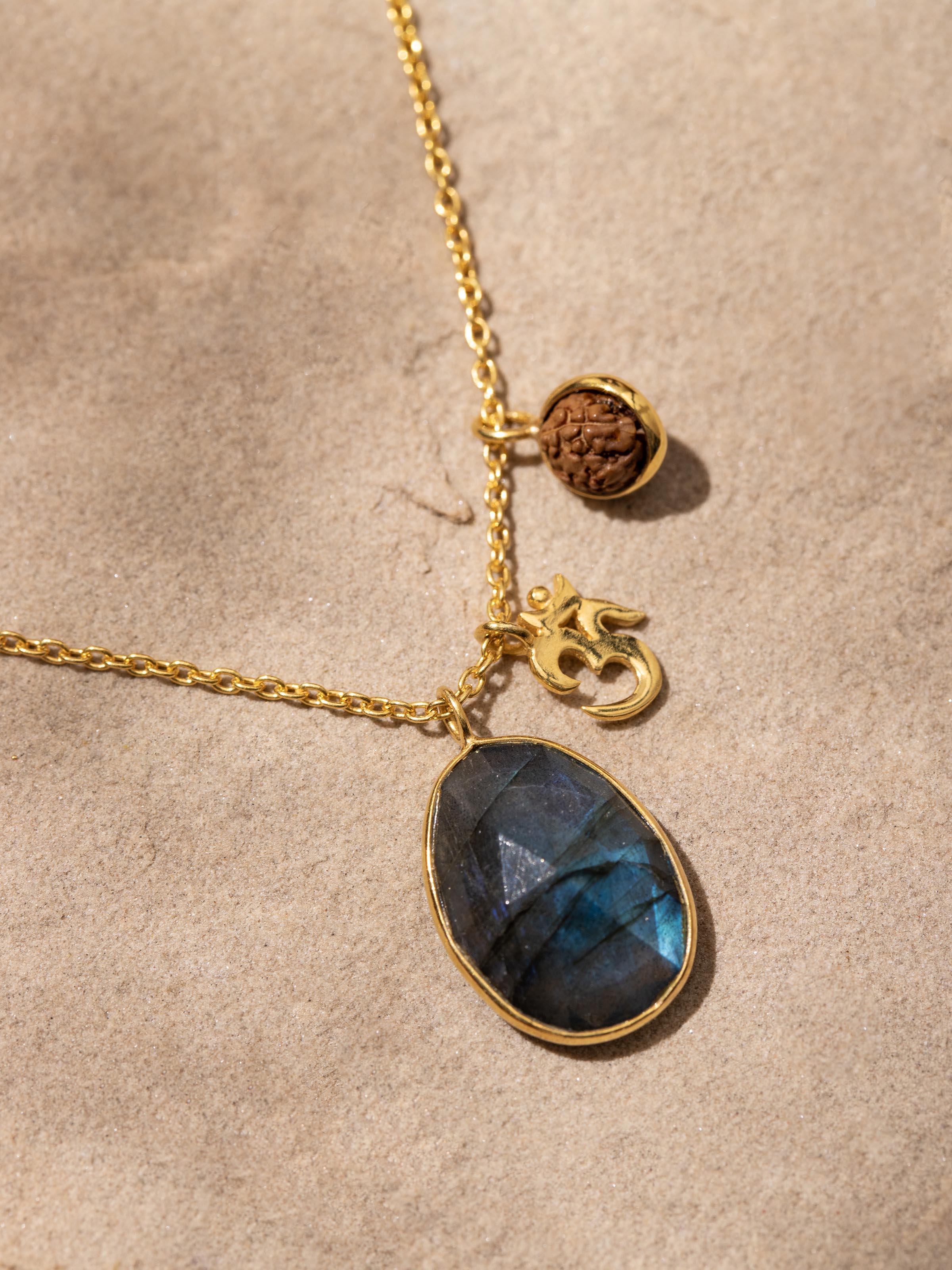 Labradorite, OM silver charm & Rudraksha necklace with 18K gold plating displayed on a surface to highlight its craftsmanship.