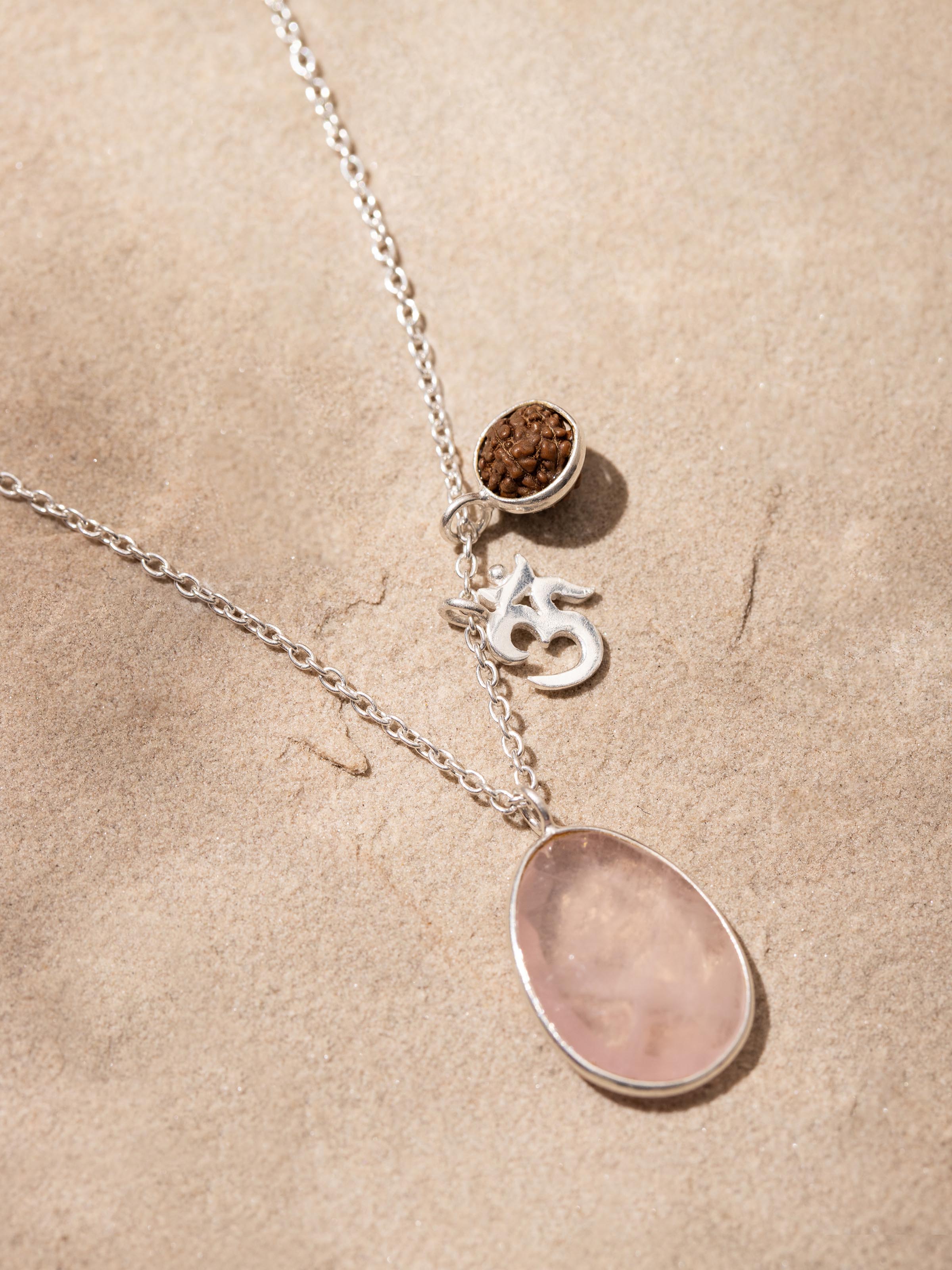 Necklace displayed on a flat surface, highlighting the combination of Rose Quartz, Om Silver Charm, and Rudraksha beads.