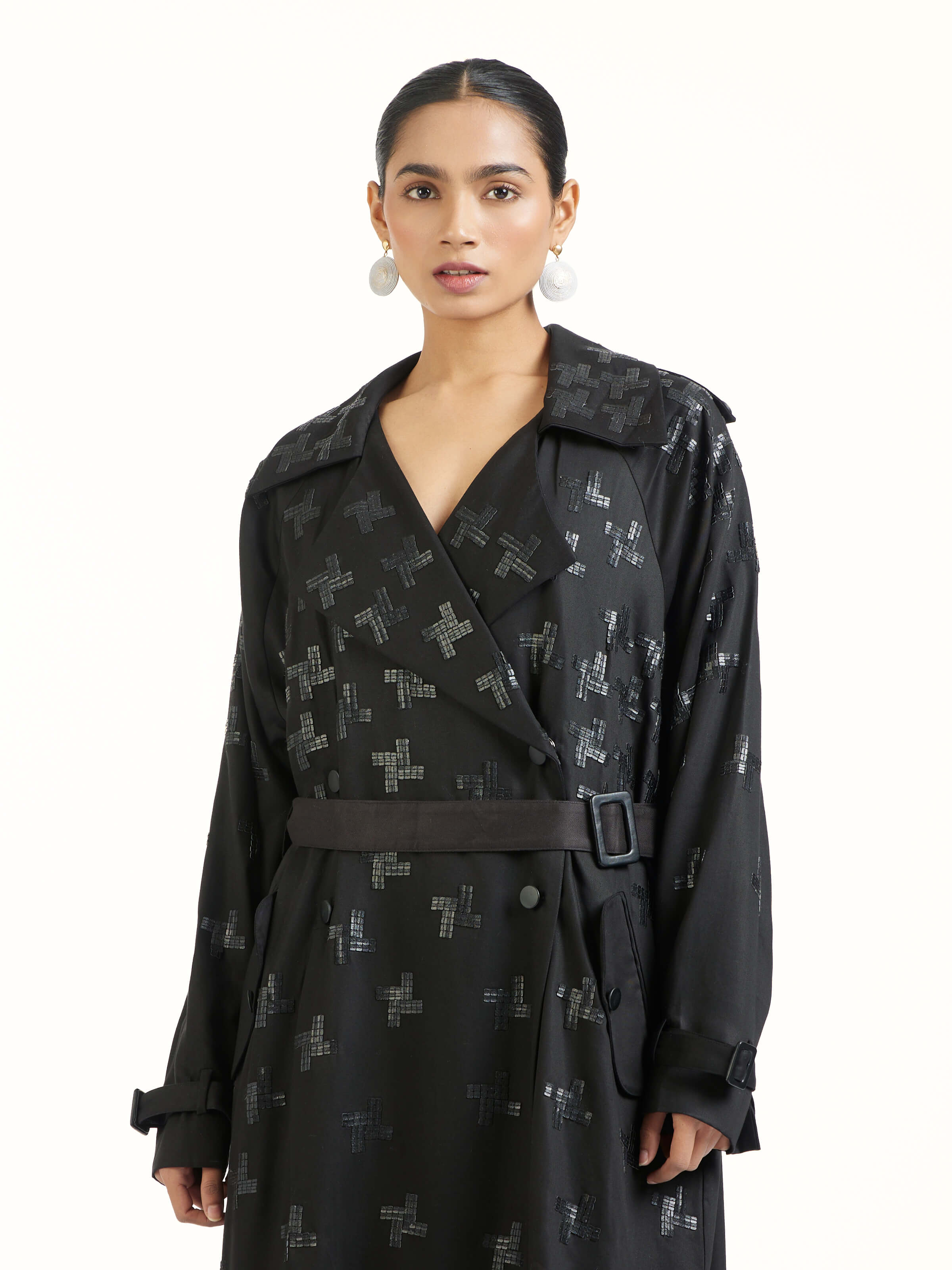 Angled view of black hand embroidered houndstooth sequin trenchcoat emphasizing texture and embellishment