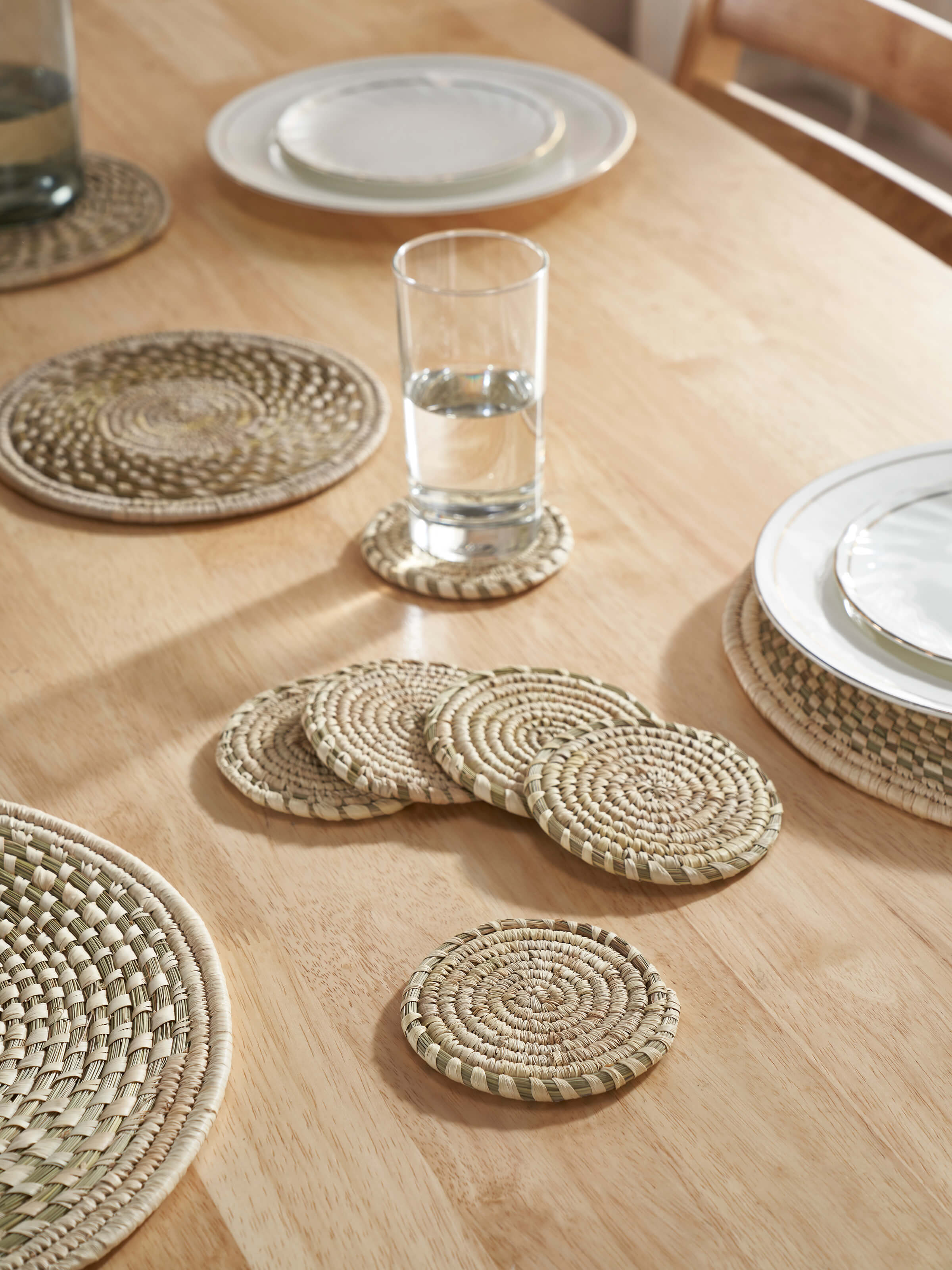 Lifestyle view of Amodini light green Sabai grass coasters arranged under glasses on a rustic wooden table.