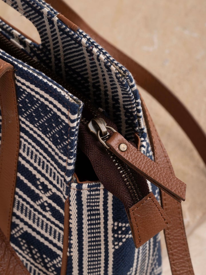 Model holding textile sling bag with strap detailing and traditional weave.