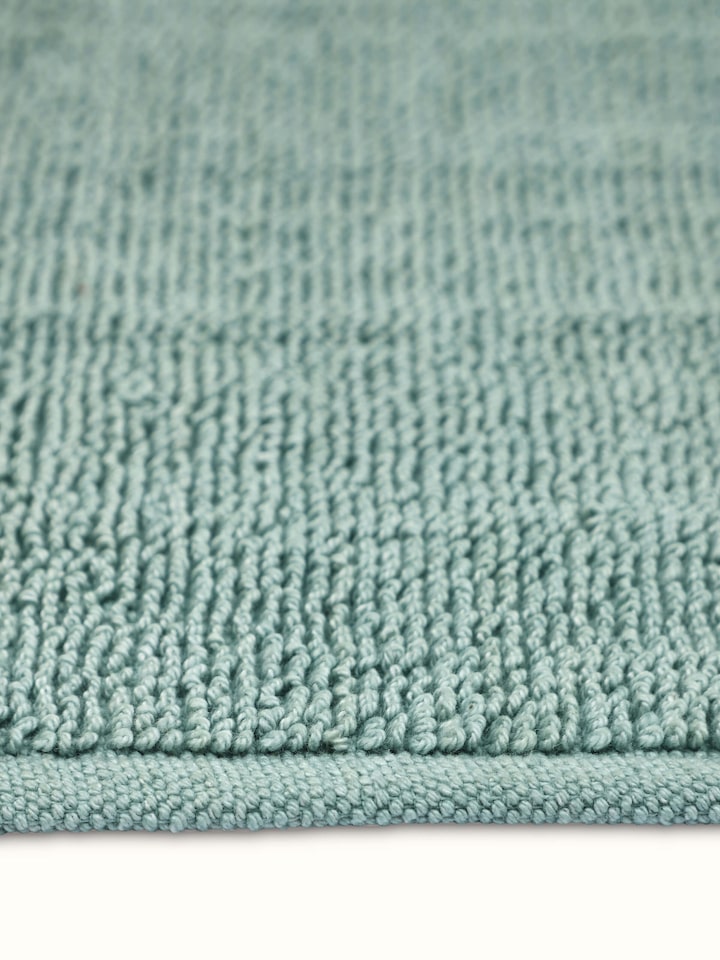 Angled view of Nityam solid light green cotton bath mat