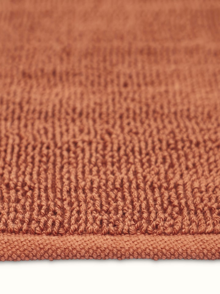 Angled view of Nityam solid rust cotton bath mat
