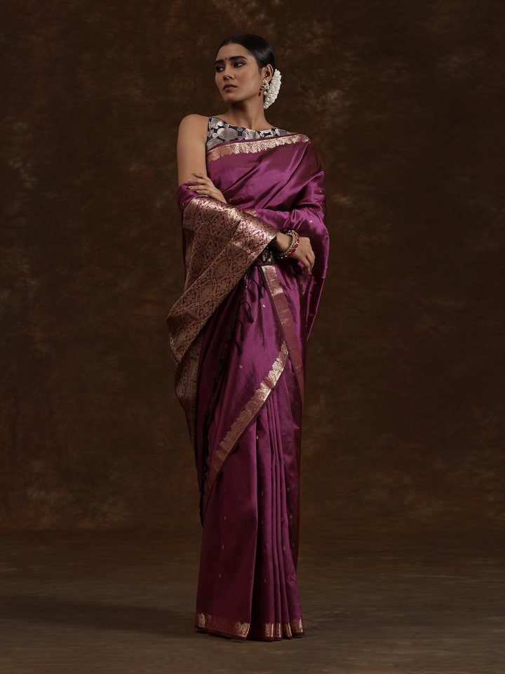 Woman posing in purple Banarasi silk saree styled with gold jewelry and festive look.