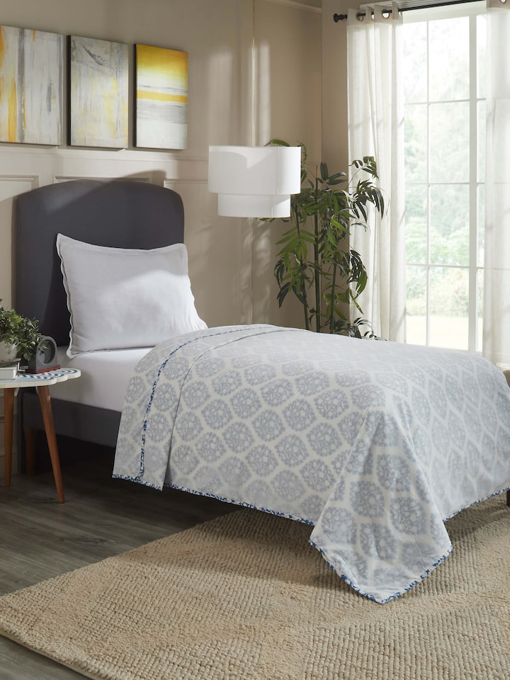 Lifestyle shot of printed dohar draped on a bed, showcasing soft cotton texture and traditional pattern.