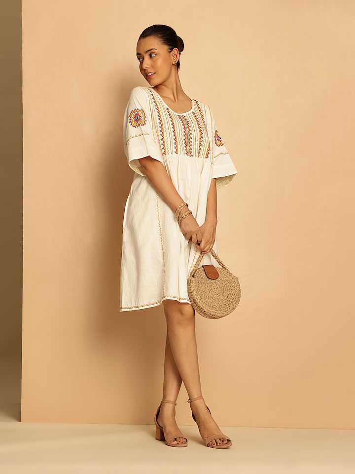 Lifestyle view of off-white short cotton Rajasthani embroidered dress worn by model highlighting embroidery details and comfortable fit.