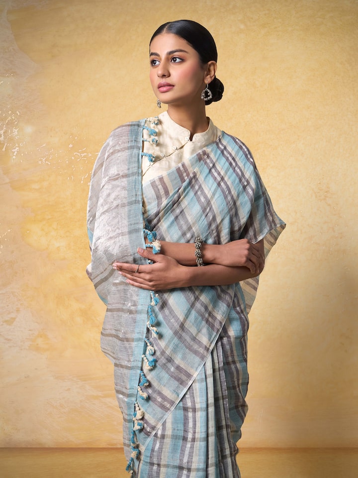 Side profile of model in grey linen saree capturing the drape and zari border in motion.
