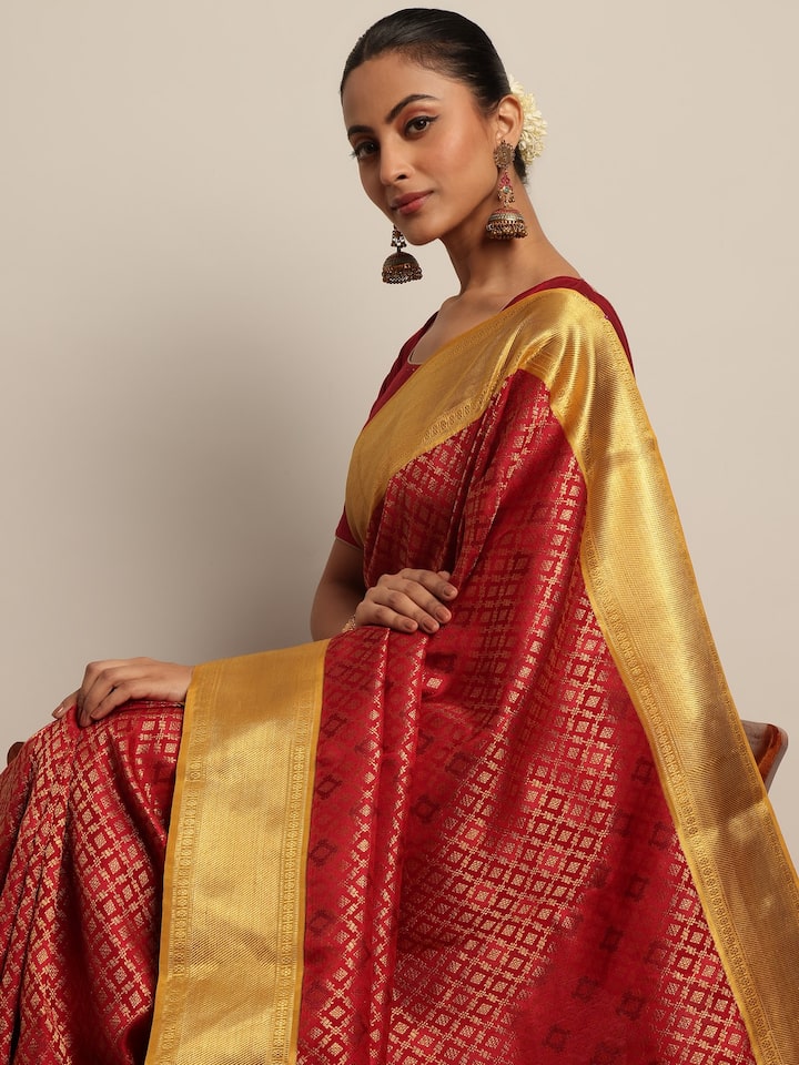 Side angled view of model wearing red silk Kancheepuram saree, emphasizing the grandeur of the woven motifs.