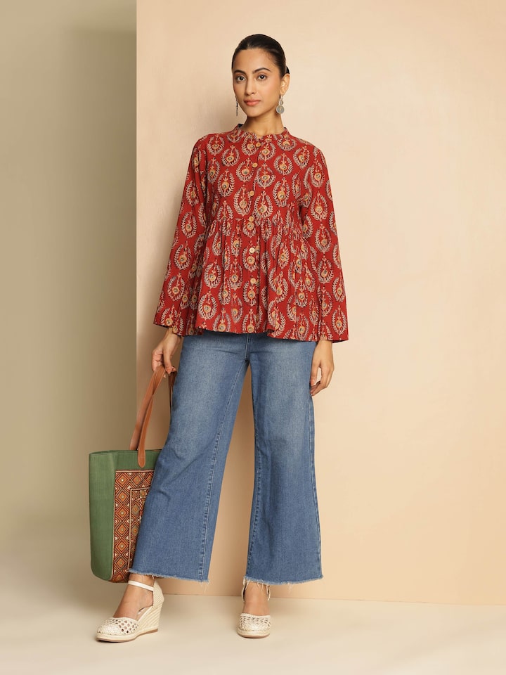 Lifestyle shot of model wearing red cotton Kalamkari block print peplum top paired with denim.