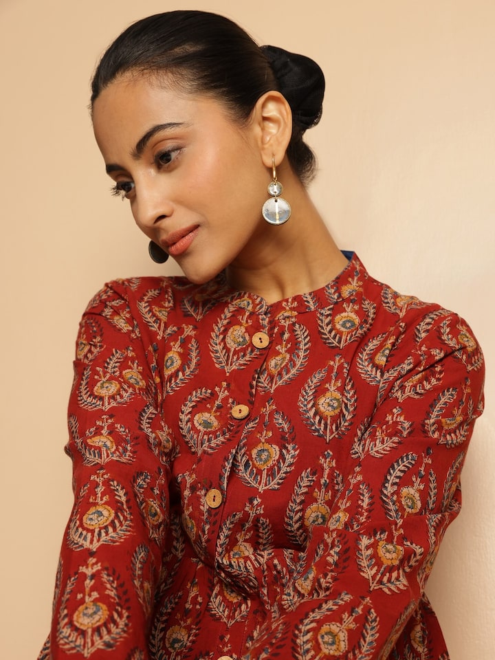 Model turning slightly to highlight the detailed print and fit of the red Kalamkari peplum top.