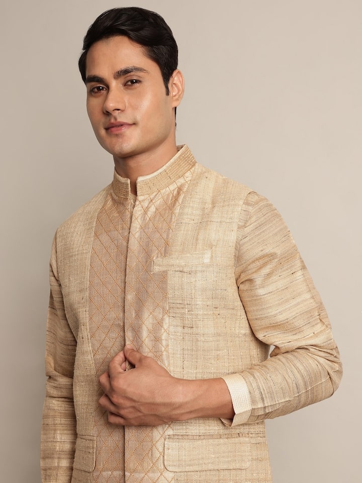 Angled view of sleeveless beige Tussar silk jacket showing neckline and hem finish.