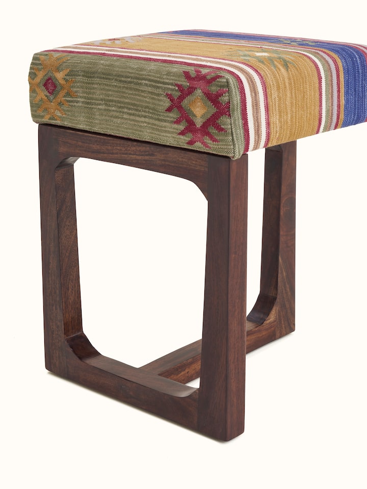 Side view of the Panja Dhurrie stool, emphasizing the combination of upholstered fabric and Sheesham wood legs