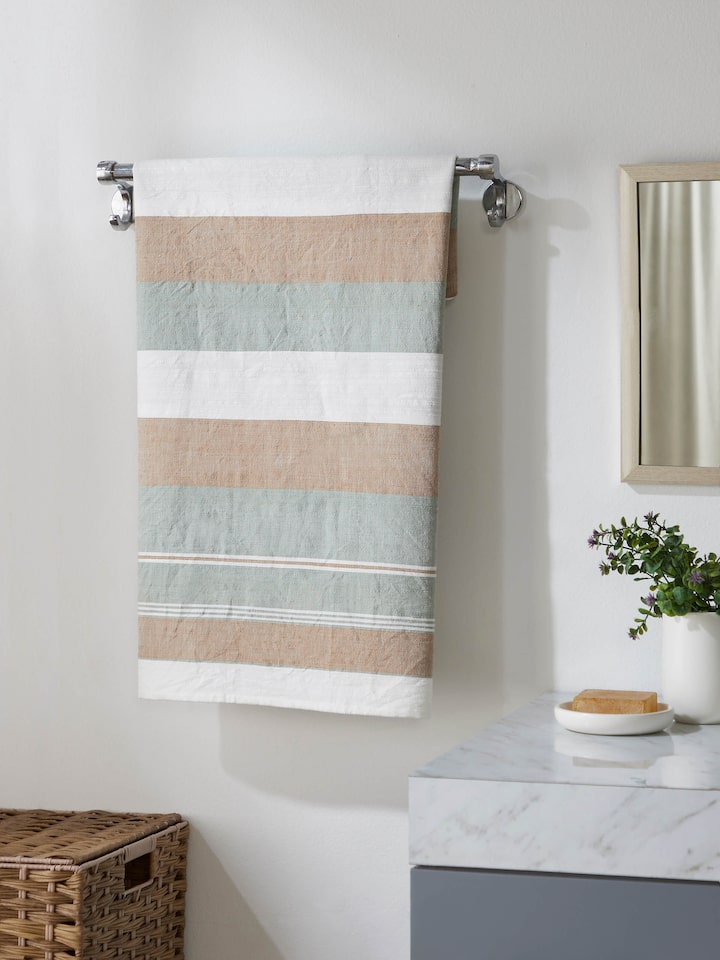 Lifestyle image of a green cotton striped bath towel, displayed in a modern bathroom setting.