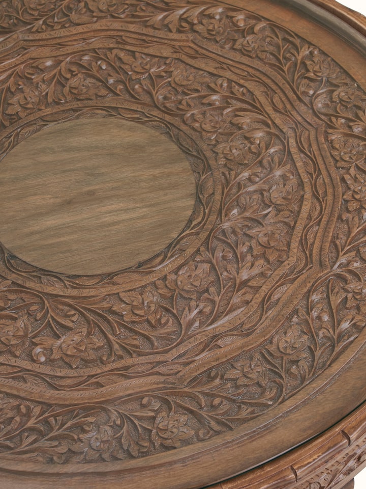 Detail view of Carved Walnut Wood Round Coffee Table with Glass Top highlighting the woodwork and finish detail, in an alternate close-up