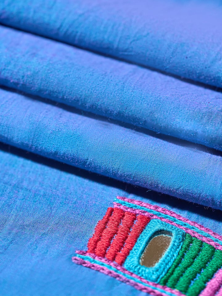 Back view of solid blue cotton blouse piece featuring traditional Lambani embroidery patterns