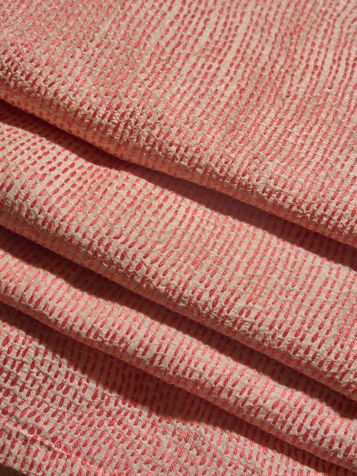 Off-white tussar silk blouse fabric laid flat showing colorful Sujani embroidery motifs.
