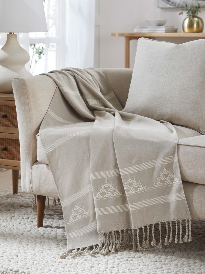Throw styled on a chair showing Godna beige cotton texture and woven stripe pattern.