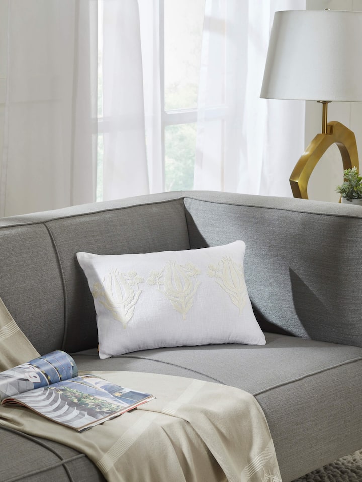 Side view of embroidered cushion cover placed on beige sofa setting