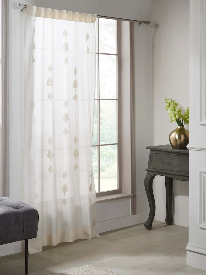 Lifestyle shot of embroidered sheer curtain hanging in a bright window setting.