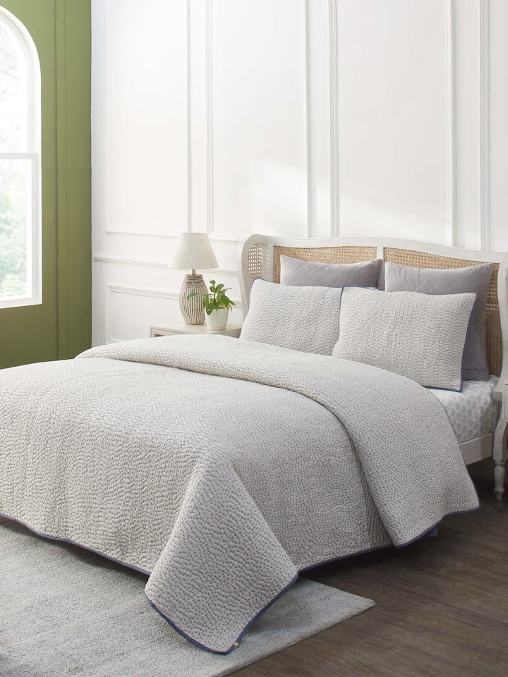 Lifestyle shot of a beige two-tone textured cotton razai embroidered double bedspread set, displayed in a bedroom setting.