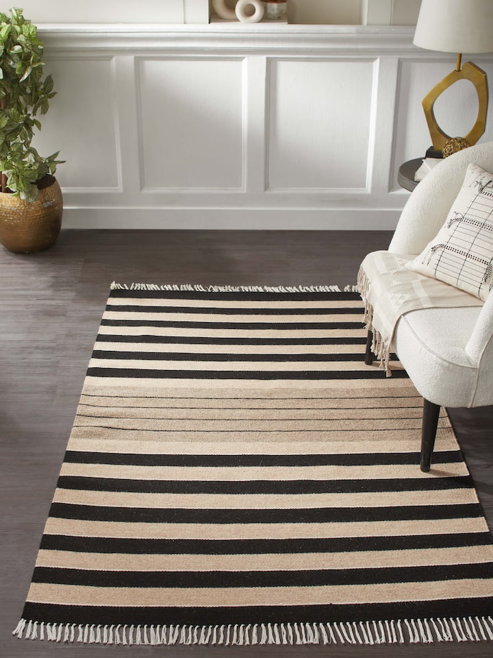 Lifestyle view of black-beige striped Jawaja wool handloom dhurrie, 4x6 ft, adding contrast to wooden flooring.