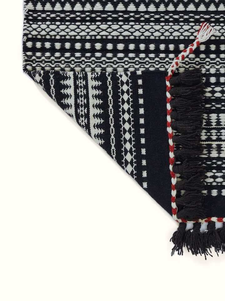 Side view of Sindhi textured ivory black salawas wool panja dhurrie, demonstrating its thickness and texture.