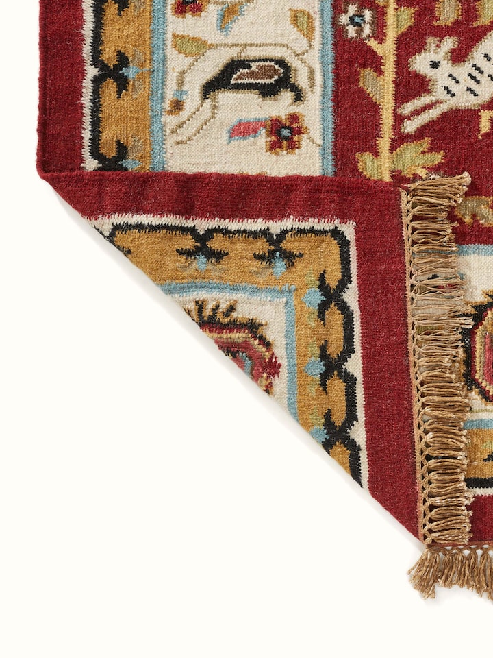 Detailed view of the Village pictorial red wool & cotton panja dhurrie, emphasizing the weaving and color patterns