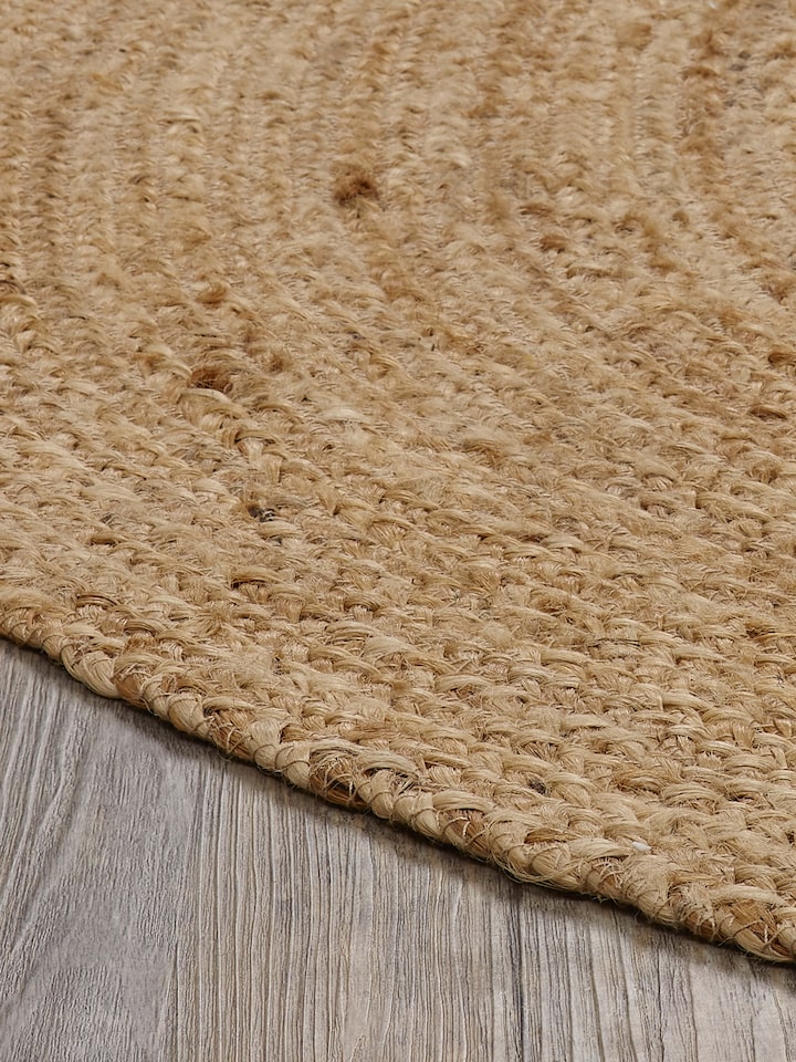 Braided round beige jute natural fibre rug, laid out to display its full round shape and texture.