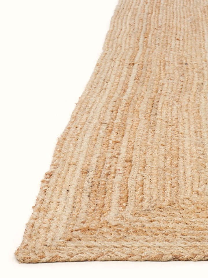 Angled view of braided concentric rectangle beige Lawan jute rug (4x6 ft), displaying its design and natural jute weave