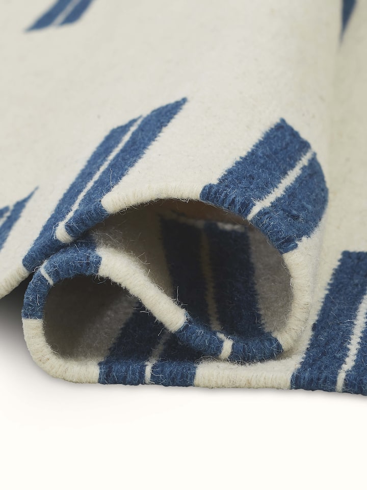 Side view of Geo Border Ivory Blue Gujarat Wool & Cotton Panja Dhurrie, showing its thickness and edge details.
