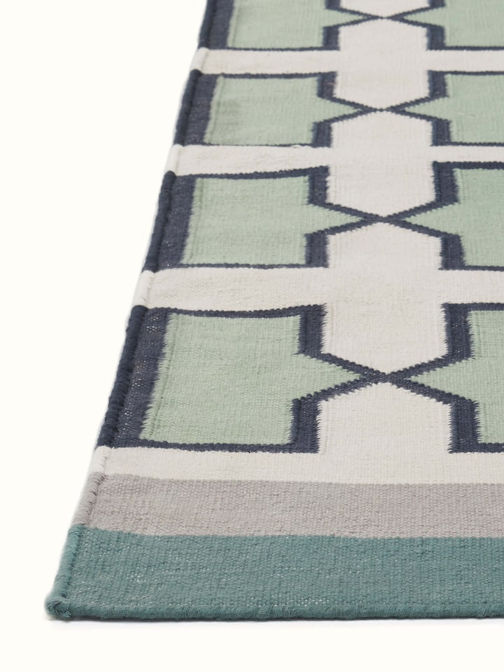 Angled view of Modern Geo Jharokha green grey Lawan cotton Panja dhurrie, illustrating its pattern and fabric drape
