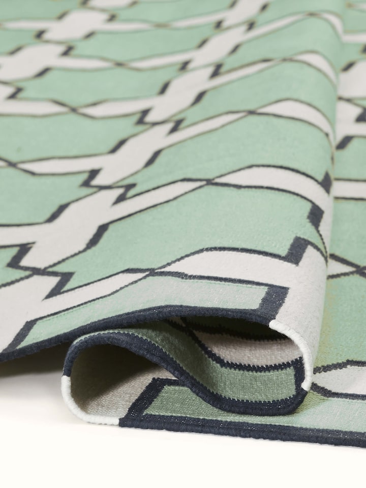 Side view of Modern Geo Jharokha green grey Lawan cotton Panja dhurrie, showing its thickness and border details