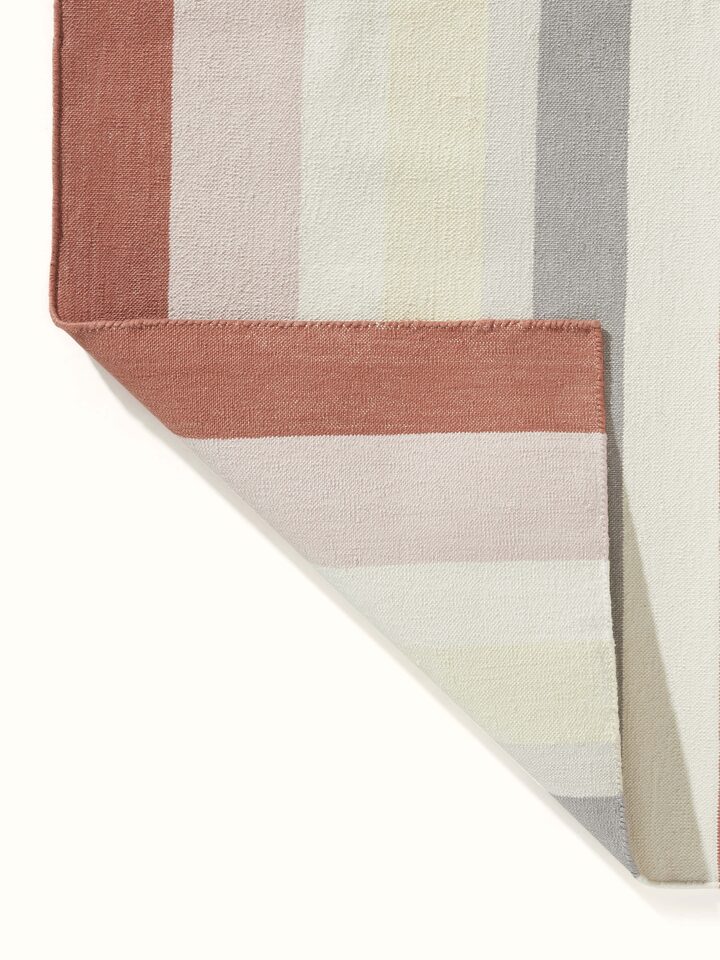 Close-up of Modern geo stripe rust lawan cotton panja dhurrie showing the texture and color variations in the fabric.