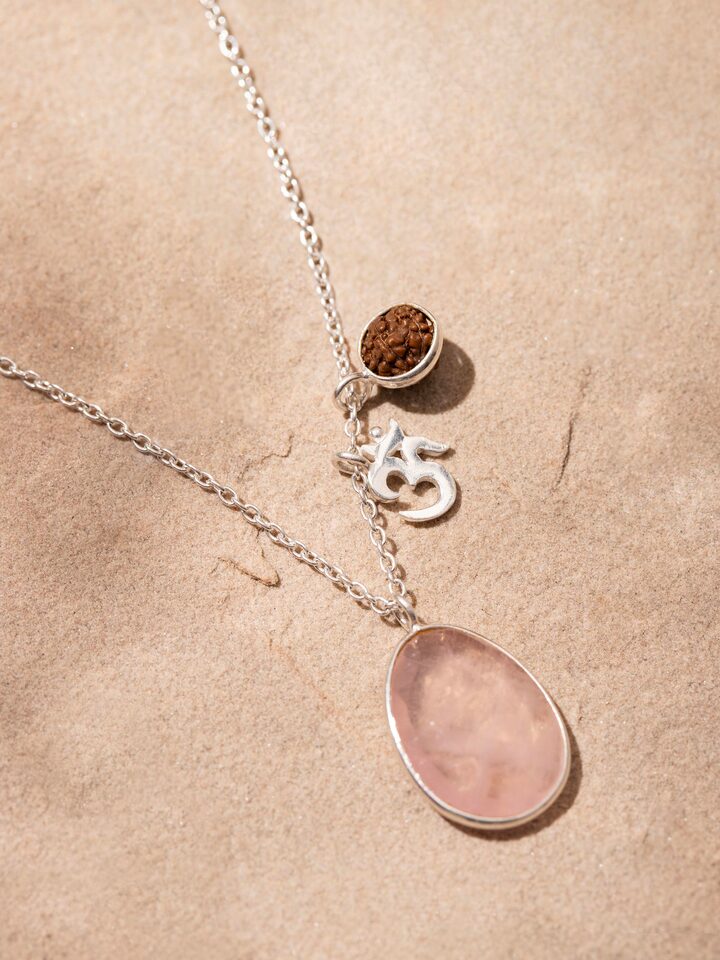Necklace displayed on a flat surface, highlighting the combination of Rose Quartz, Om Silver Charm, and Rudraksha beads.