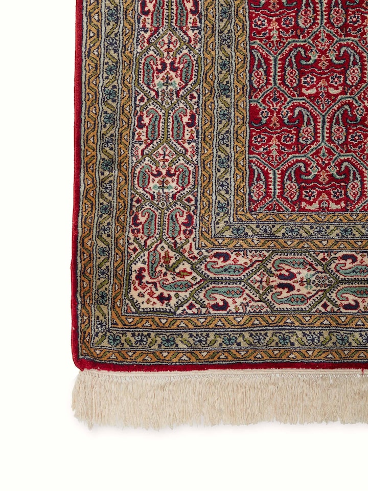 Angled view of Traditional Persian Red Senna Kashmir Silk Hand-Knotted Carpet emphasizing the detailed craftsmanship and color variations.